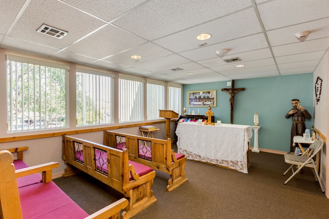 A small chapel interior featuring wooden pews, an altar, and a cross on the wall.