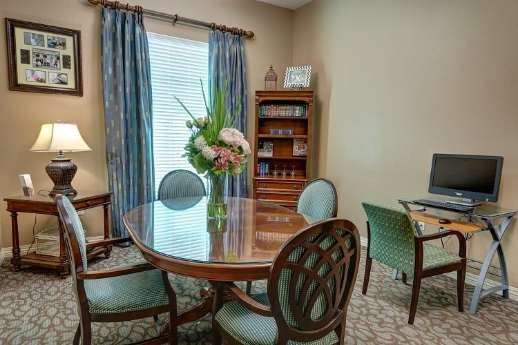 A small office meeting room with a round table, chairs, bookshelf, and floral arrangement.