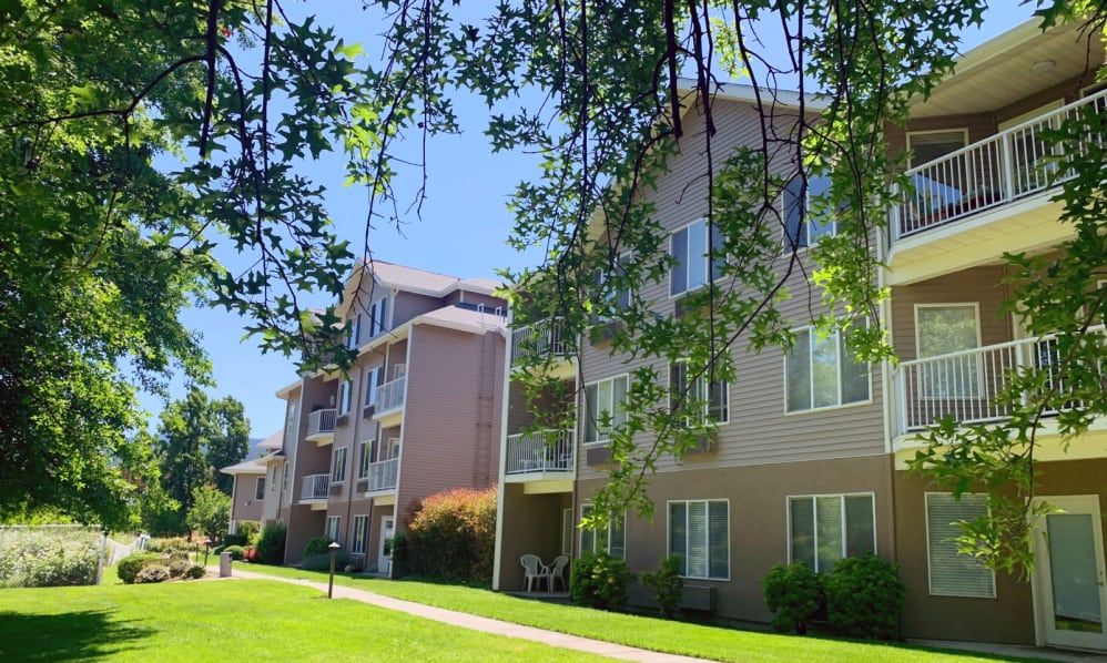 View of a residential apartment building surrounded by trees and greenery on a sunny day.