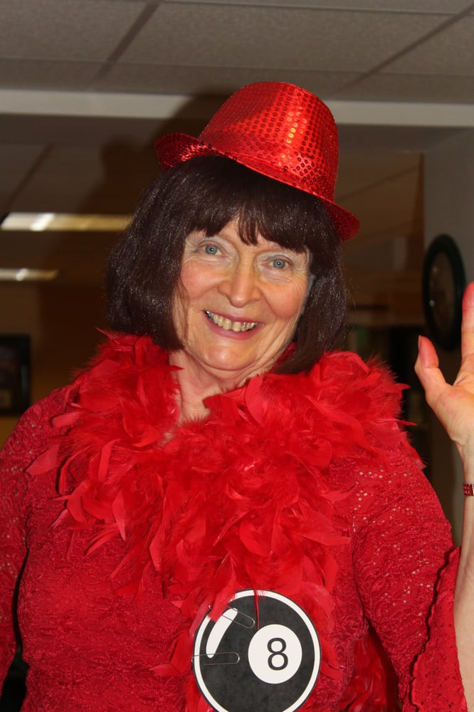 A woman wearing a red hat and boa, smiling indoors.