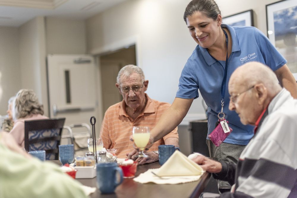 A caregiver serving a drink to senior citizens during meal time at a nursing home.