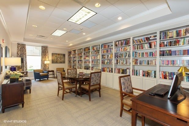 A cozy library with bookshelves, tables, and chairs in a well-lit reading area.