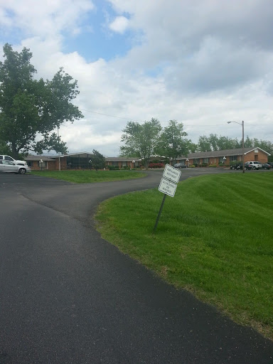 A view of a curved road bordered by grass and trees, featuring a sign that appears to be leaning.