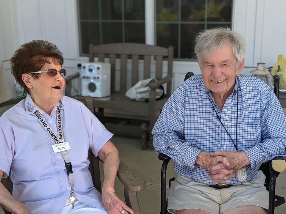 Two elderly individuals sitting outdoors and smiling.