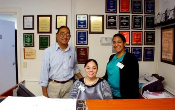 A group of three people smiling in an office with award plaques on the wall.