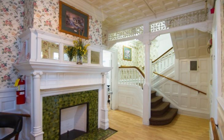 A cozy, vintage interior featuring a fireplace with tile details and a classic staircase adorned with wallpaper and wood accents.