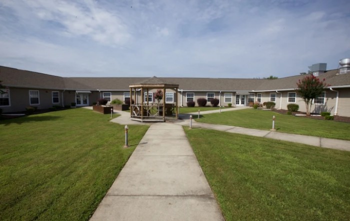 A courtyard with a central gazebo and pathways surrounded by a building and well-maintained lawns.