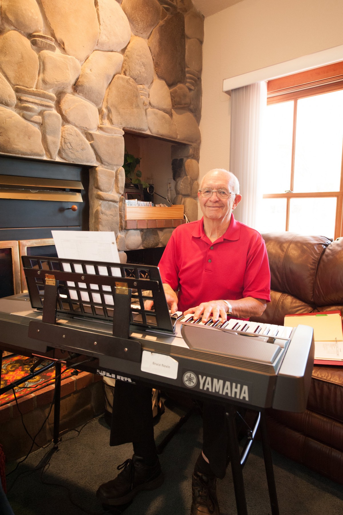 A man in a red shirt playing a Yamaha keyboard in a cozy living room.