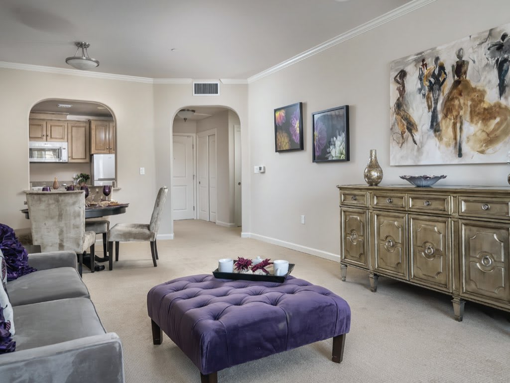 A stylish living room with a purple ottoman and elegant decor leading into a dining area.