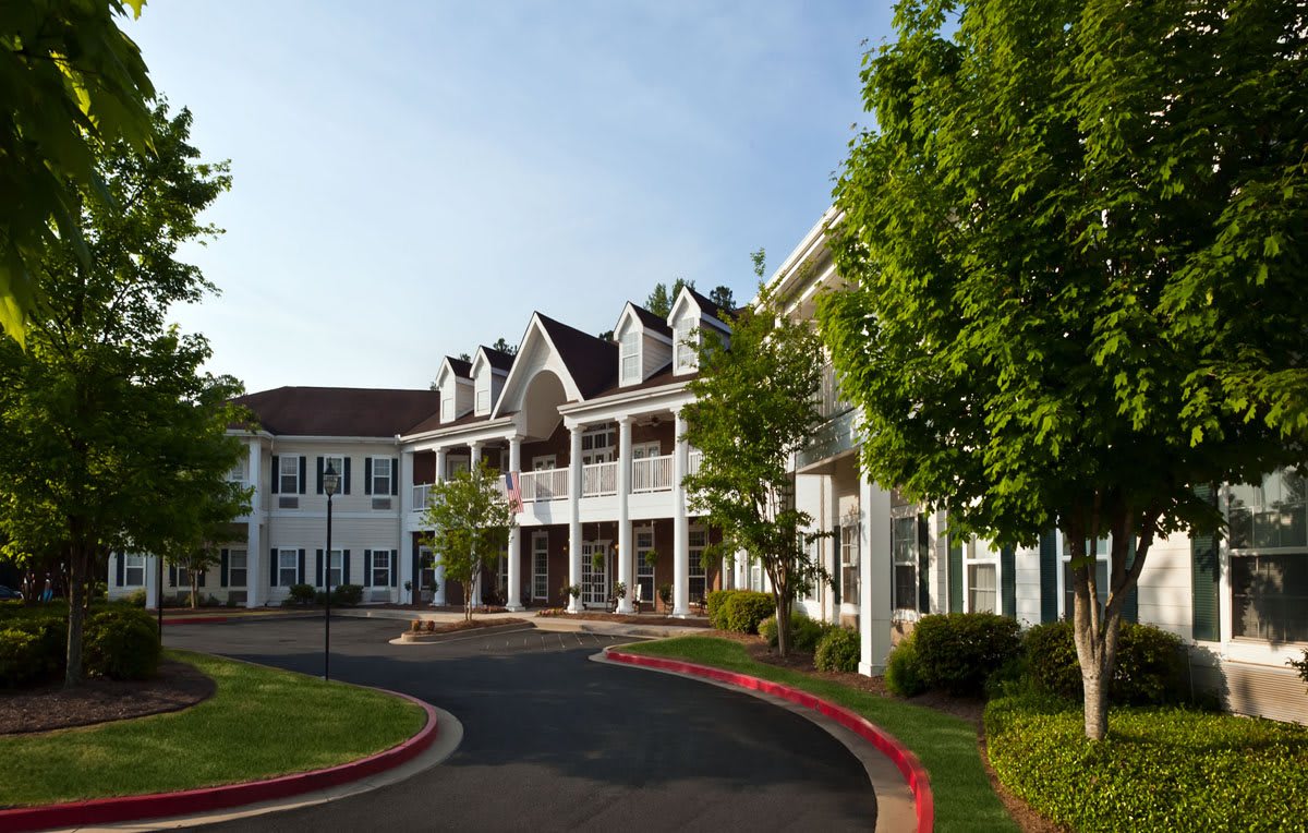 A scenic view of a large building with white exterior and green trees lining the entrance.