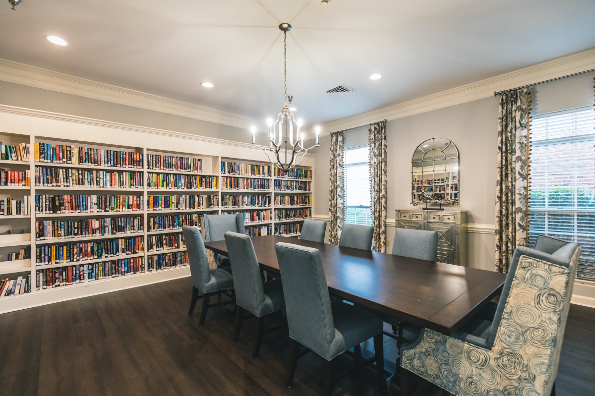 A cozy library and dining room with bookshelves lining the walls and a large table beneath a chandelier.