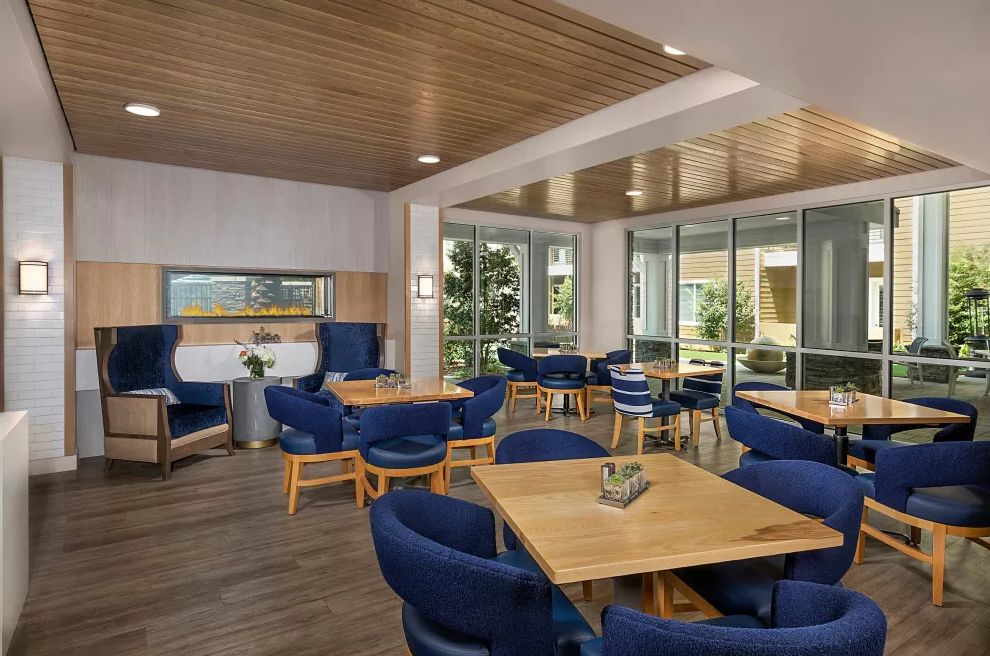 A modern lounge area featuring blue chairs and wooden tables, with a stylish wood-paneled ceiling.