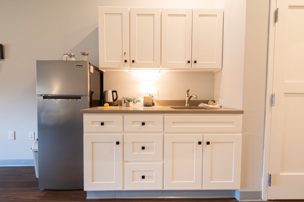 A compact kitchen setup with white cabinets, a countertop, sink, and a small refrigerator.