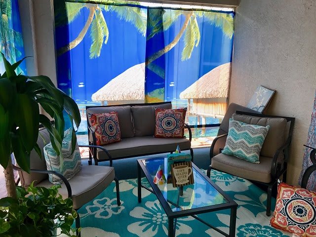 A cozy patio seating area with tropical-themed decor, featuring colorful cushions and a glass table.