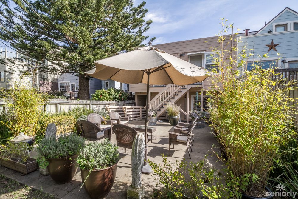 A well-furnished backyard patio with a large umbrella, surrounded by lush plants.