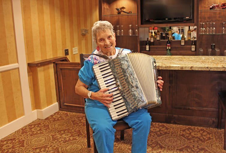An elderly person playing an accordion indoors with a smile.
