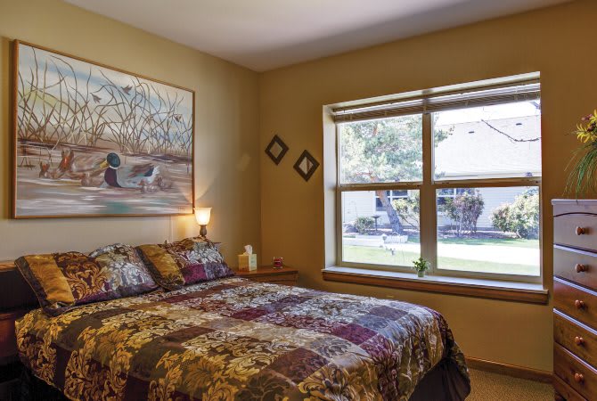 A cozy bedroom featuring a large bed, artwork on the wall, and a window with natural light.