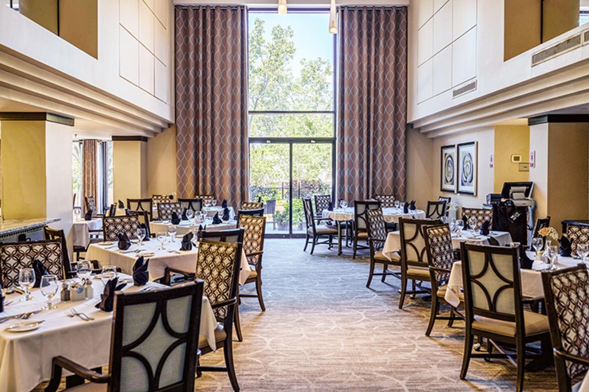 A spacious and elegantly designed restaurant dining area with neatly arranged tables and chairs, well-lit by natural light from large windows.