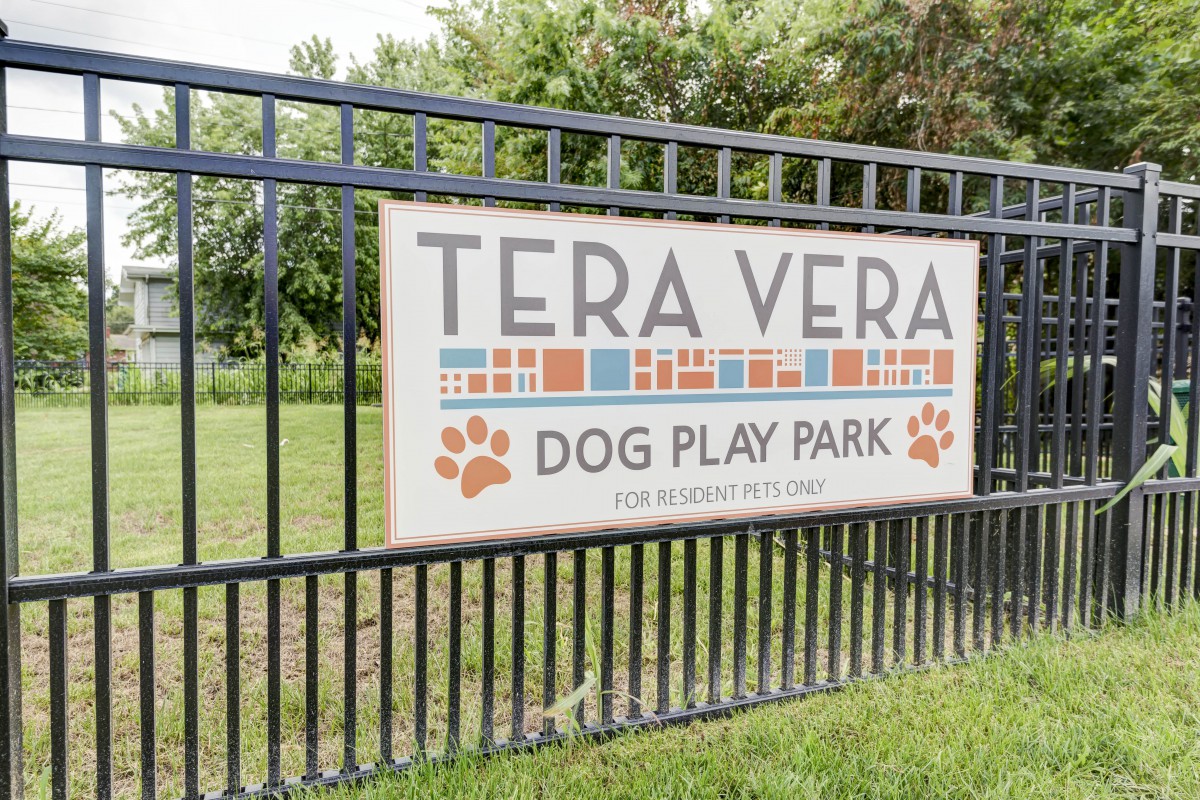 A sign for Tera Vera Dog Play Park displayed on a metal fence in an outdoor setting.