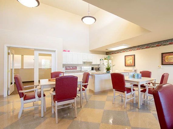 A bright, spacious dining area with red chairs and a kitchen in the background.