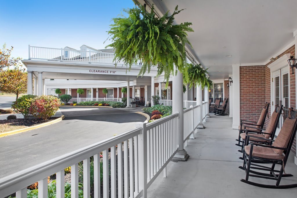 A serene porch with hanging plants and rocking chairs overlooking a driveway.