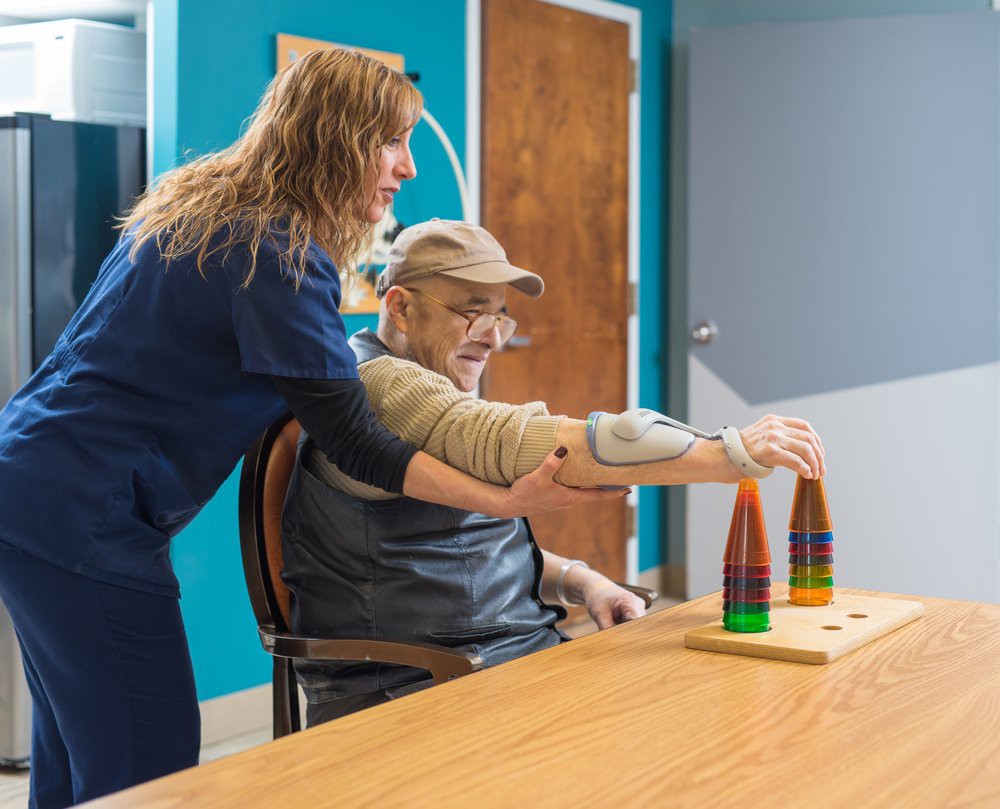 A caregiver assists an elderly person during a physical therapy session.