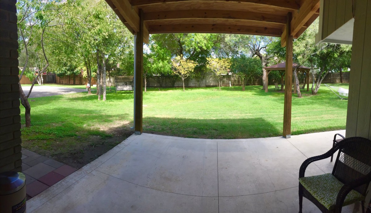 A view from a covered patio overlooking a lush green backyard with trees.