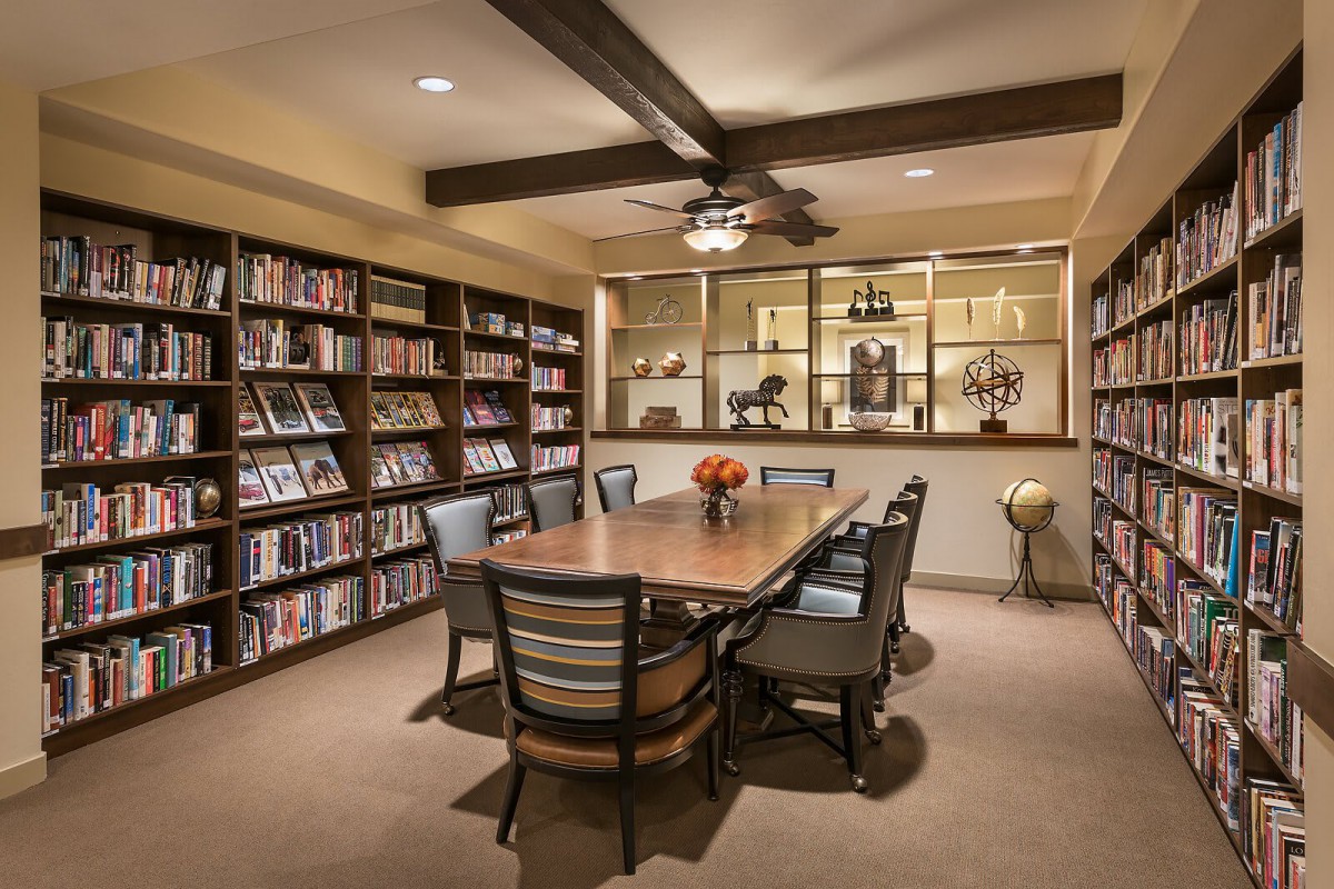 A cozy library room with a central table surrounded by chairs and bookshelves.