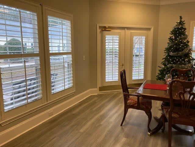A cozy dining room with plantation shutters, wood flooring, and a festive Christmas tree near the table.