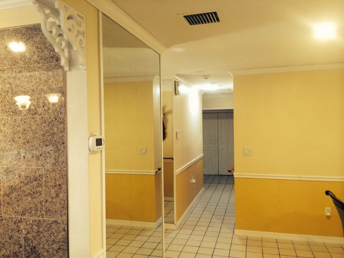 A hallway with yellow walls and tiled flooring, featuring a large wall mirror.