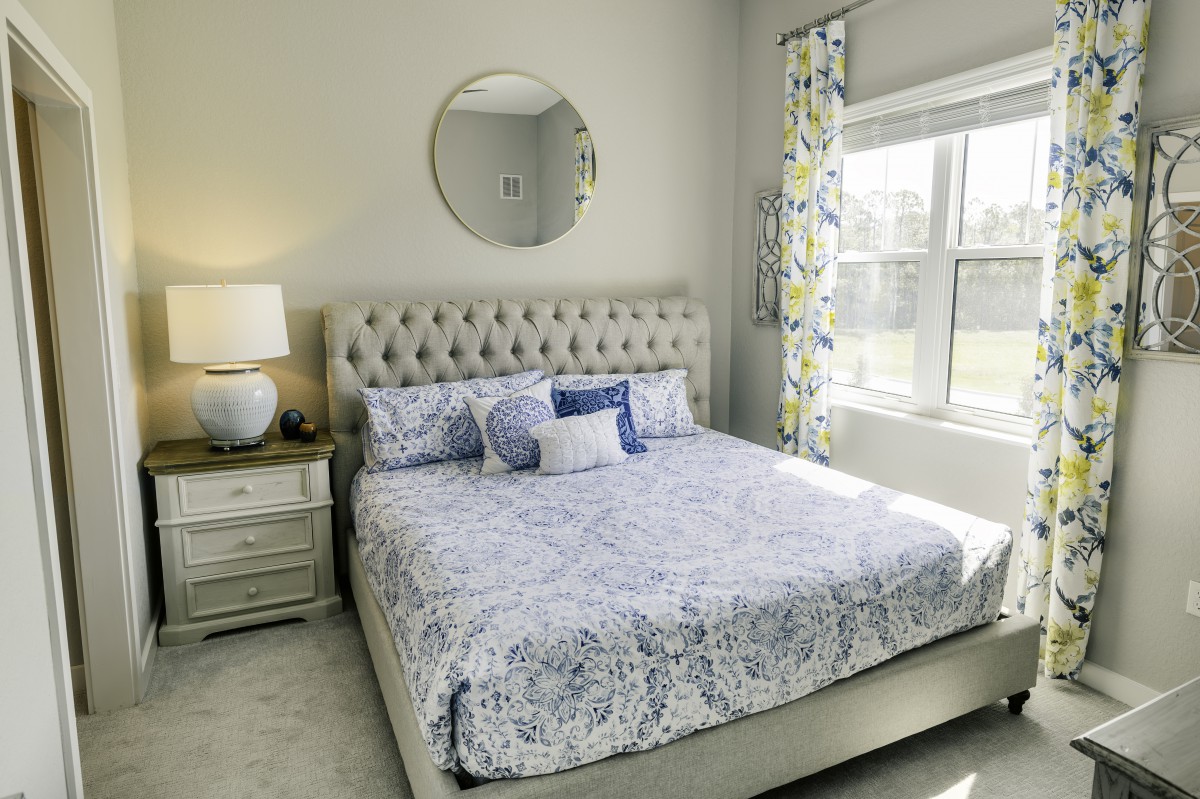 A cozy bedroom featuring a tufted bed with patterned bedding, a round mirror above the headboard, and a lamp on the bedside table.