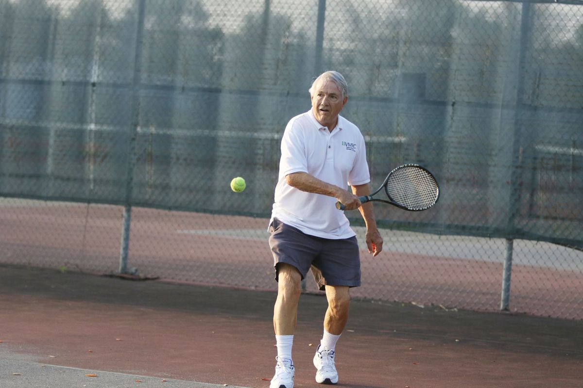 A senior man playing tennis on an outdoor court.