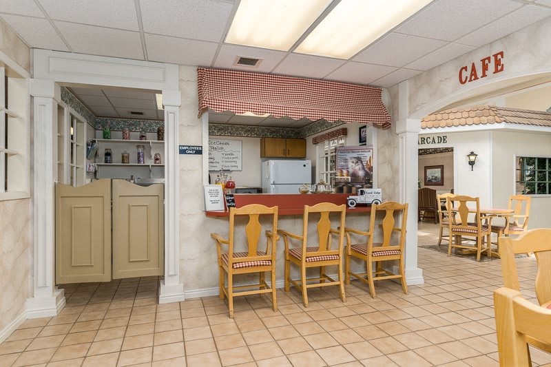 A cozy restaurant interior featuring a counter with wooden chairs and a view into the kitchen area.