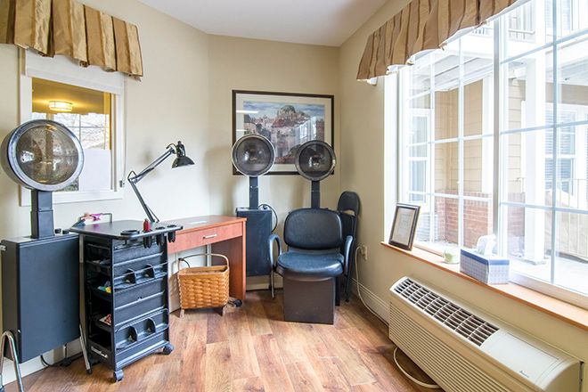 A cozy hair salon corner with a seating area, styling chair, and equipment by a sunny window.