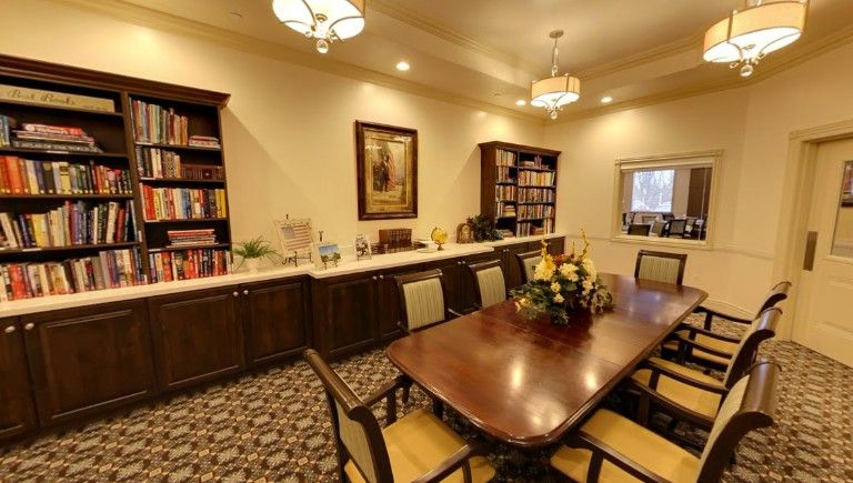 A well-furnished conference room featuring a long table, several chairs, bookshelves, and decorative elements.