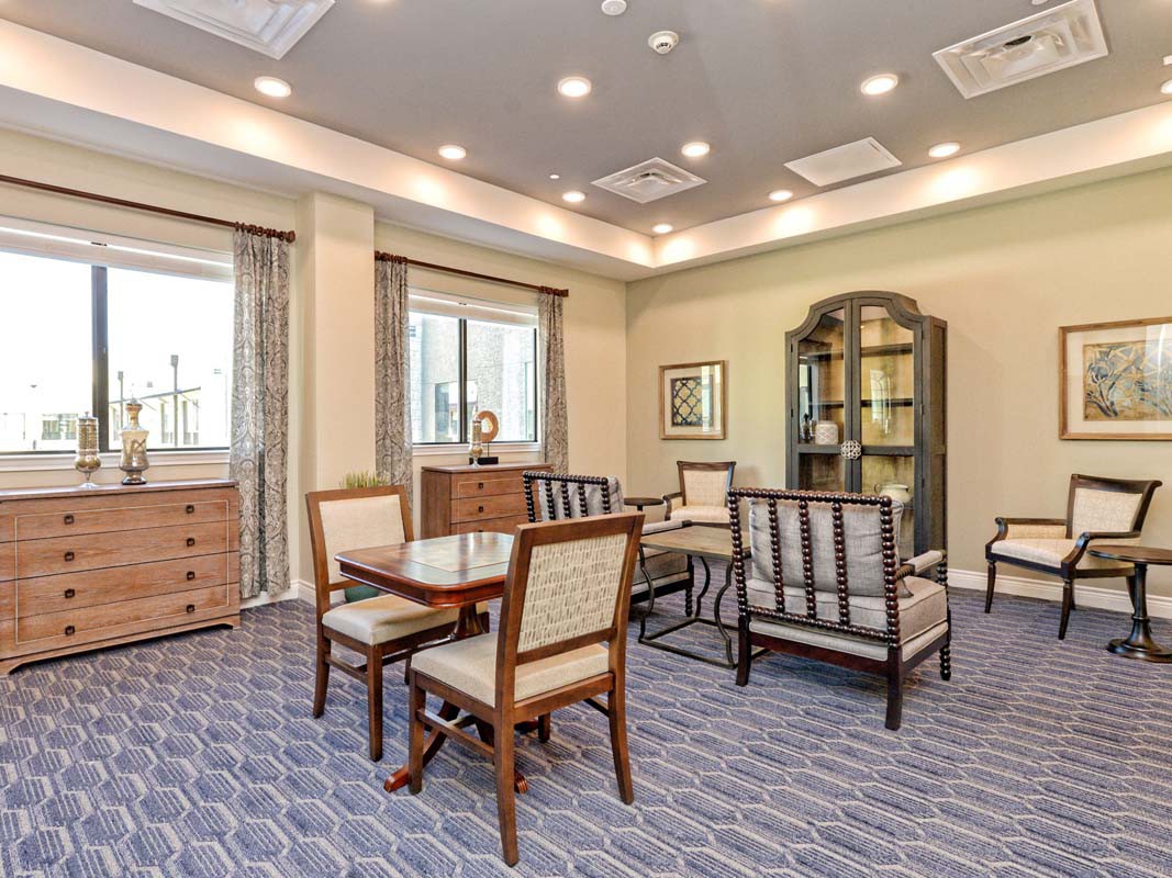 A well-furnished living area with chairs, a table, and a bookshelf under warm lighting.