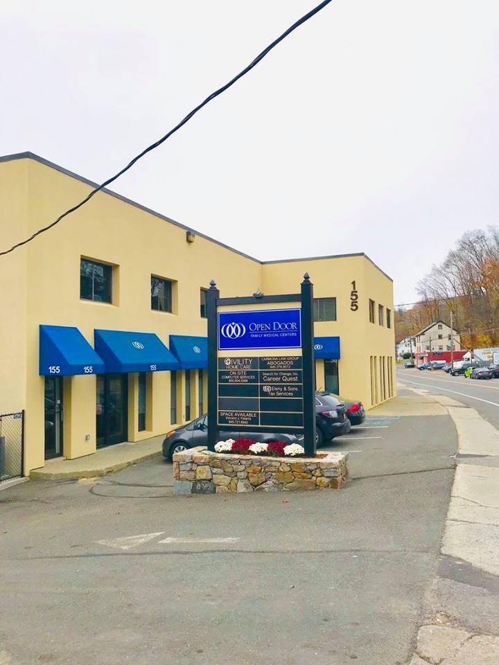 A commercial building with blue awnings and a business sign in the parking lot on an overcast day.