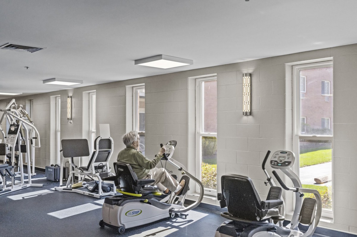 A well-lit gym with fitness equipment and a person working out on a machine.