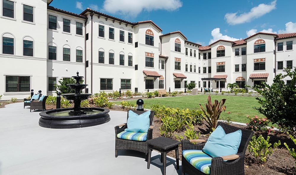 A sunny day view of a residential building with outdoor seating and a fountain in the landscaped courtyard.