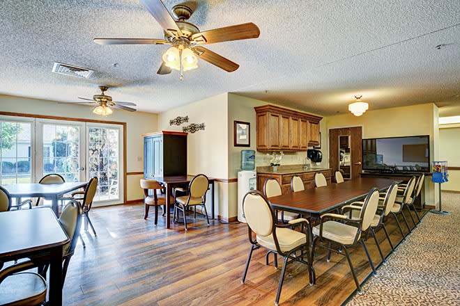 A spacious dining area with wooden floors and ceiling fans, featuring a large dining table and chairs adjacent to an open kitchen.