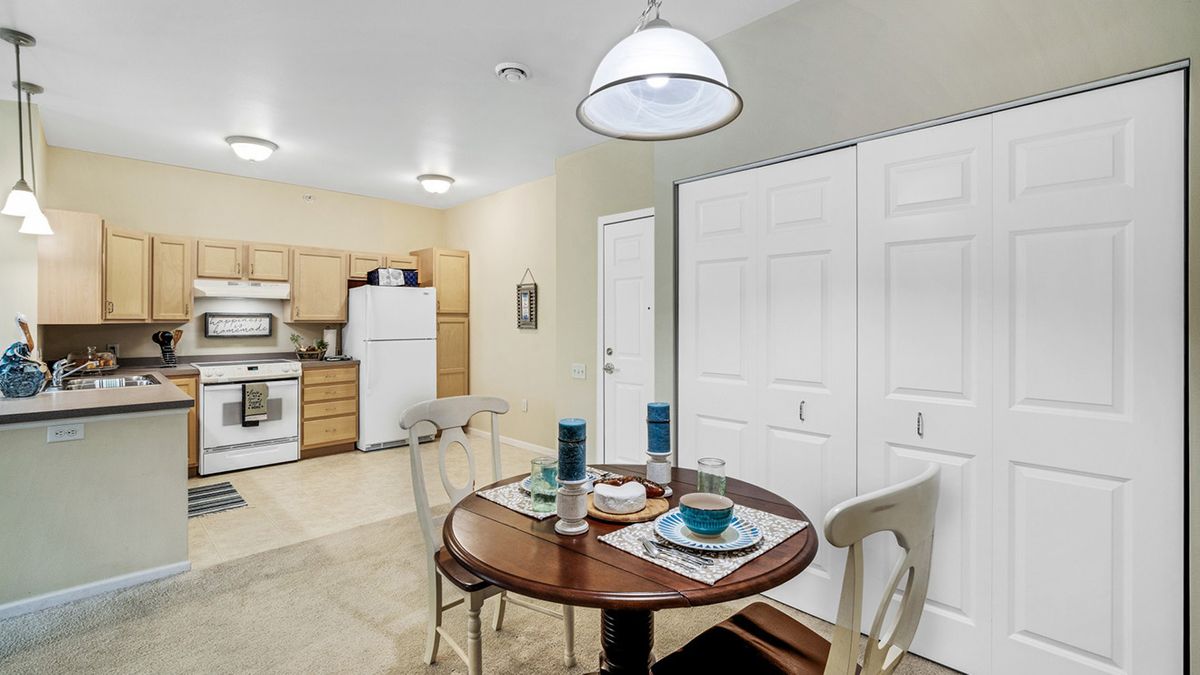 A cozy kitchen and dining area with a round table set for two, featuring modern lighting and wood cabinetry.