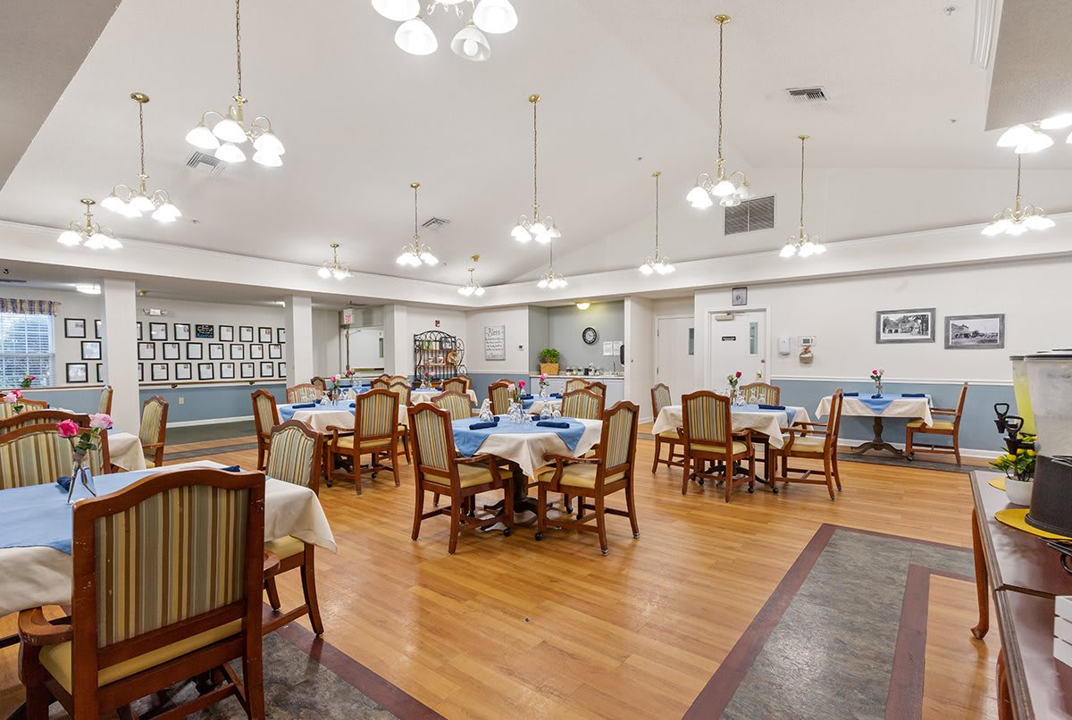 A spacious dining room with neatly arranged tables and chairs, bright lighting, and a polished wooden floor.