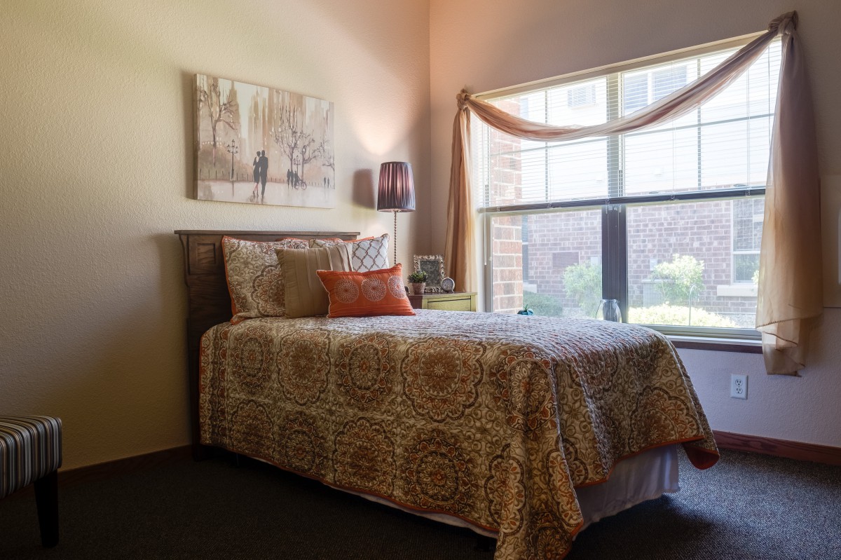 A cozy bedroom with a single bed near a window, decorated with warm tones and artwork.