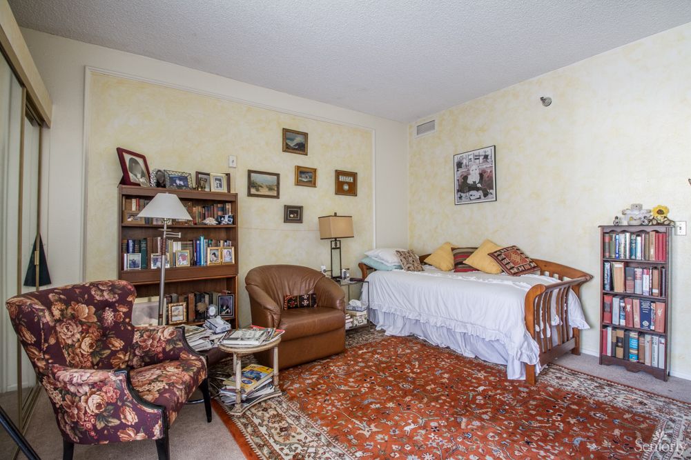 A cozy living room with vintage decor, featuring a daybed, armchair, and a patterned carpet.