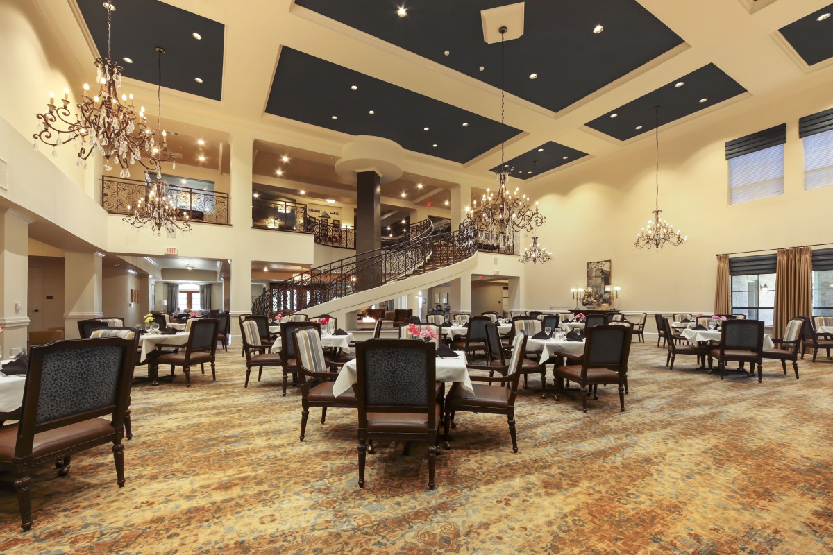 A spacious and elegantly designed restaurant dining area with chandeliers and neatly arranged tables and chairs.