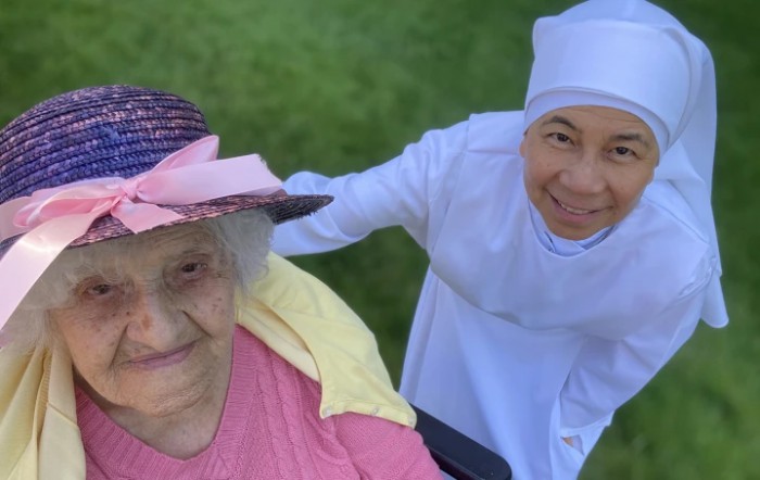 An elderly woman and a nun smiling outdoors together.