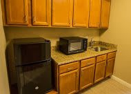 A compact kitchen with wooden cabinets, a microwave, a small refrigerator, and a sink.