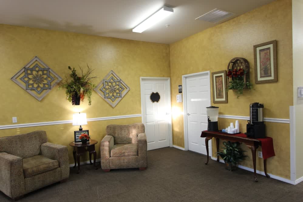A cozy waiting room with yellow walls, adorned with artwork and plants, featuring comfortable seating.