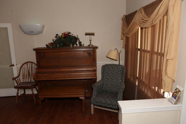 A cozy corner featuring an upright piano and a comfortable chair with a floor lamp beside it, adorned with decorative curtains.