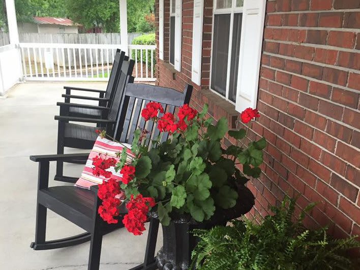 A cozy porch with black rocking chairs and vibrant red geraniums in a pot.
